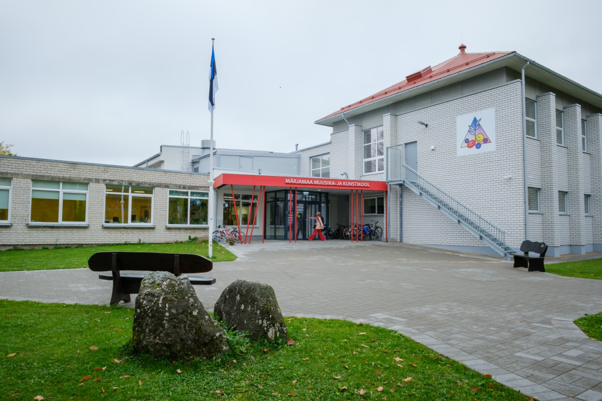 Valge telliskivist hoone ees on punase servaga varikatus ja punased tugipostid.